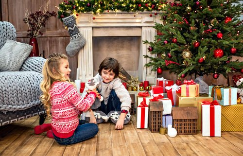 A young girl and boy opening presents under the Christmas tree fireplace with stockings hung