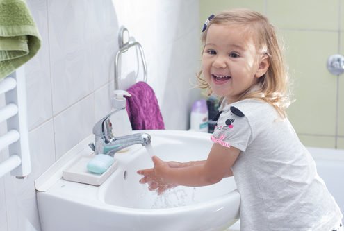 smiling happy toddler washing her hands at a bathroom sink
