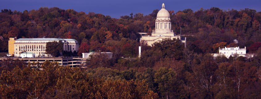A distant shot of the FrankFort Kentucky State Capitol building and Governor's mansion with a blue sky in the background and fall trees all around