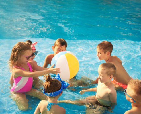 young kids playing with a beach ball in the pool