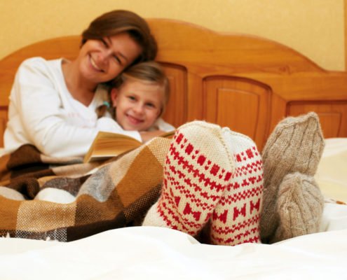 Mom and daughter lying on the bed in knitted socks reading