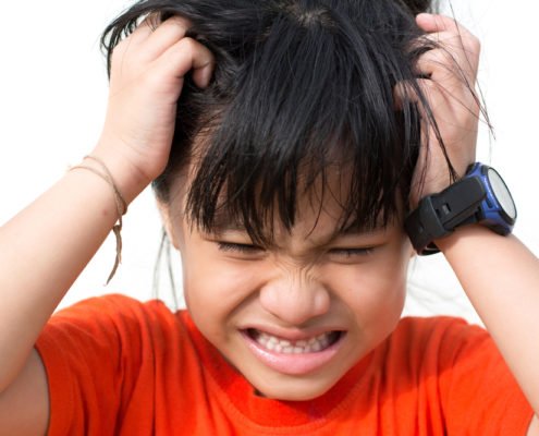 Little kid scratching their head making a irritated face because they have head lice