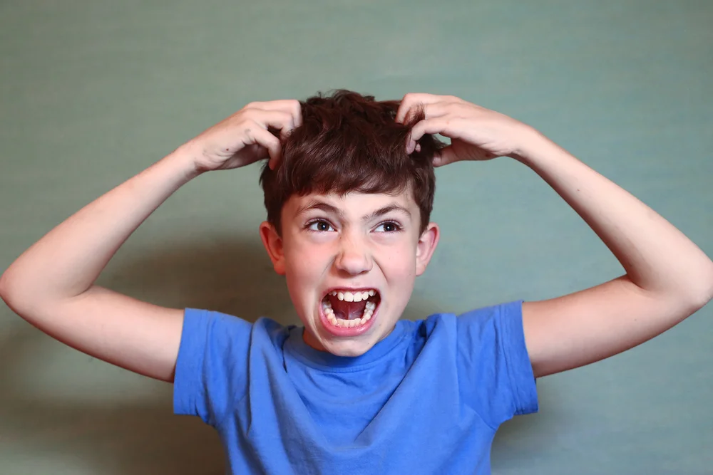 Young boy is upset he needs a head check because he may have lice wearing a blue t-shirt